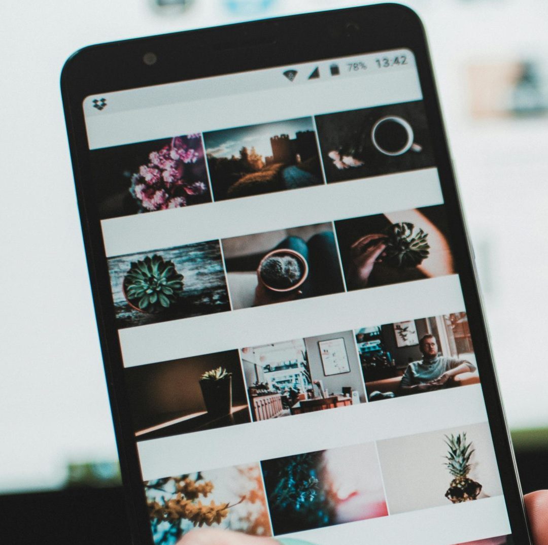 A person uses a smartphone to browse social media in front of a laptop, emphasizing modern technology and lifestyle.