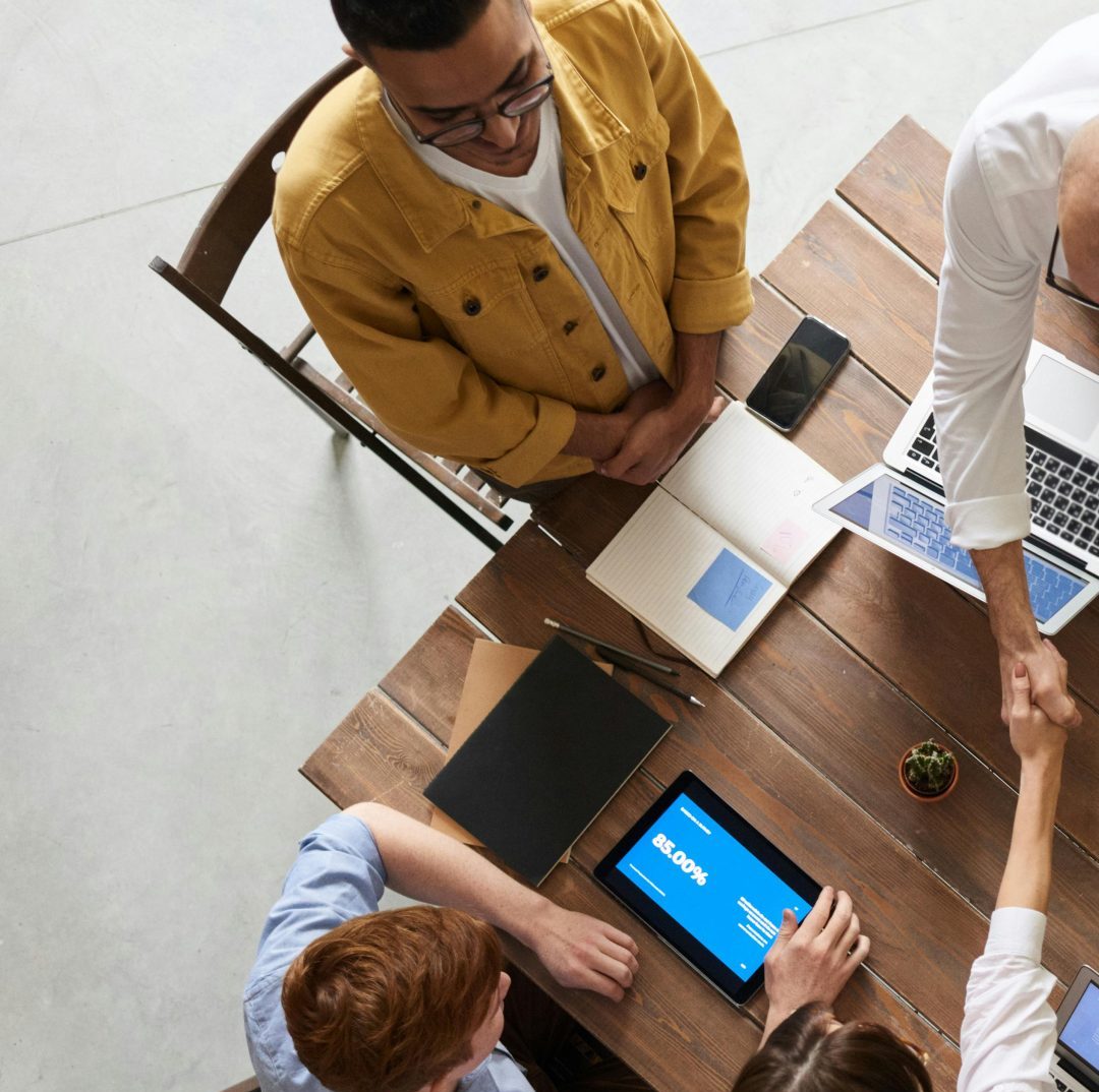 Top view of a diverse team collaborating in an office setting with laptops and tablets, promoting cooperation.