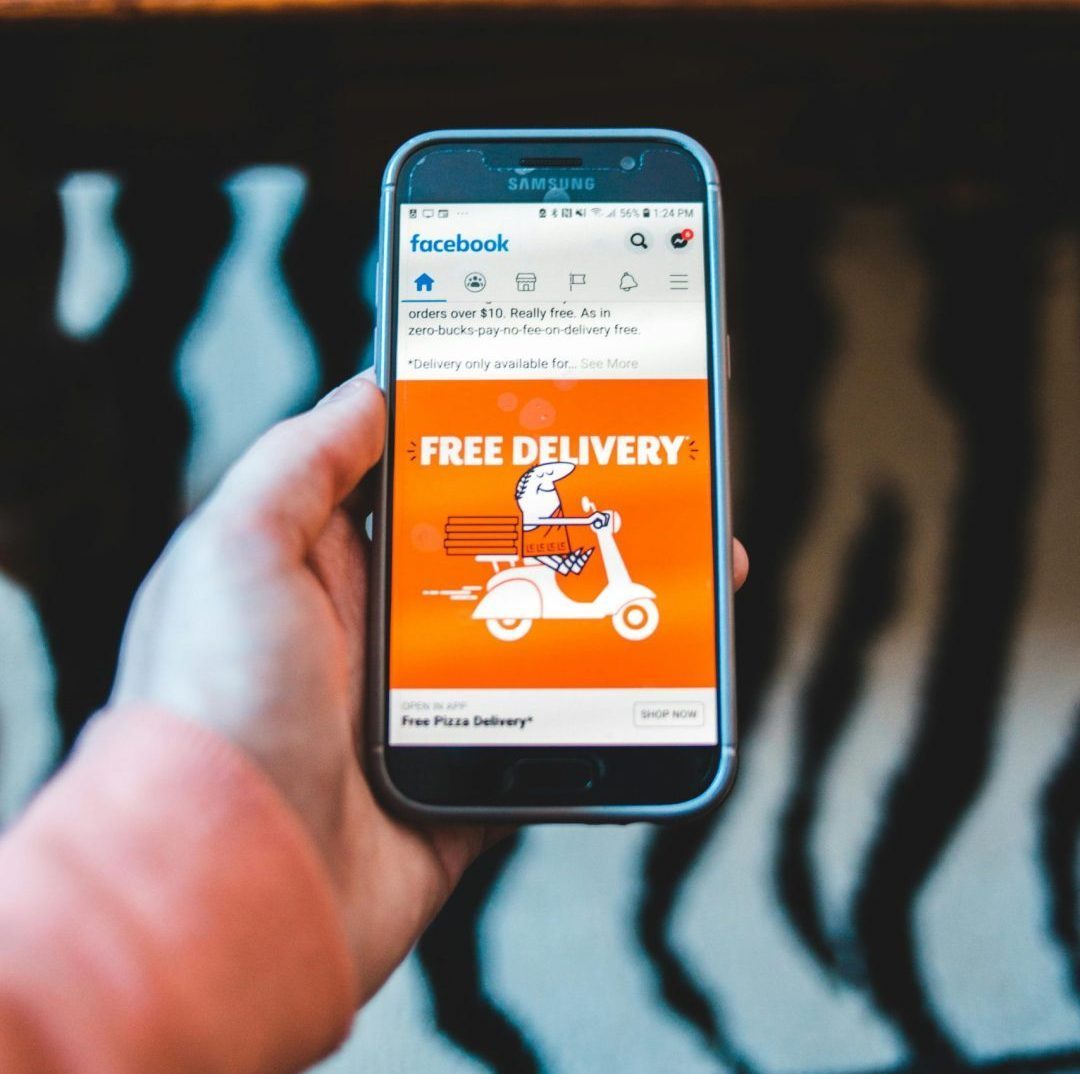 Hand holding a smartphone displaying a Facebook ad for free delivery, capturing modern digital communication.